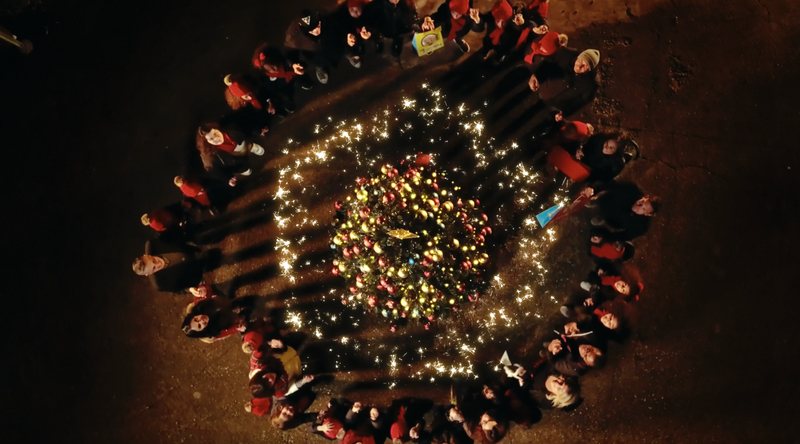 Ripresa dall'alto di persone in cerchio attorno a un albero di luci